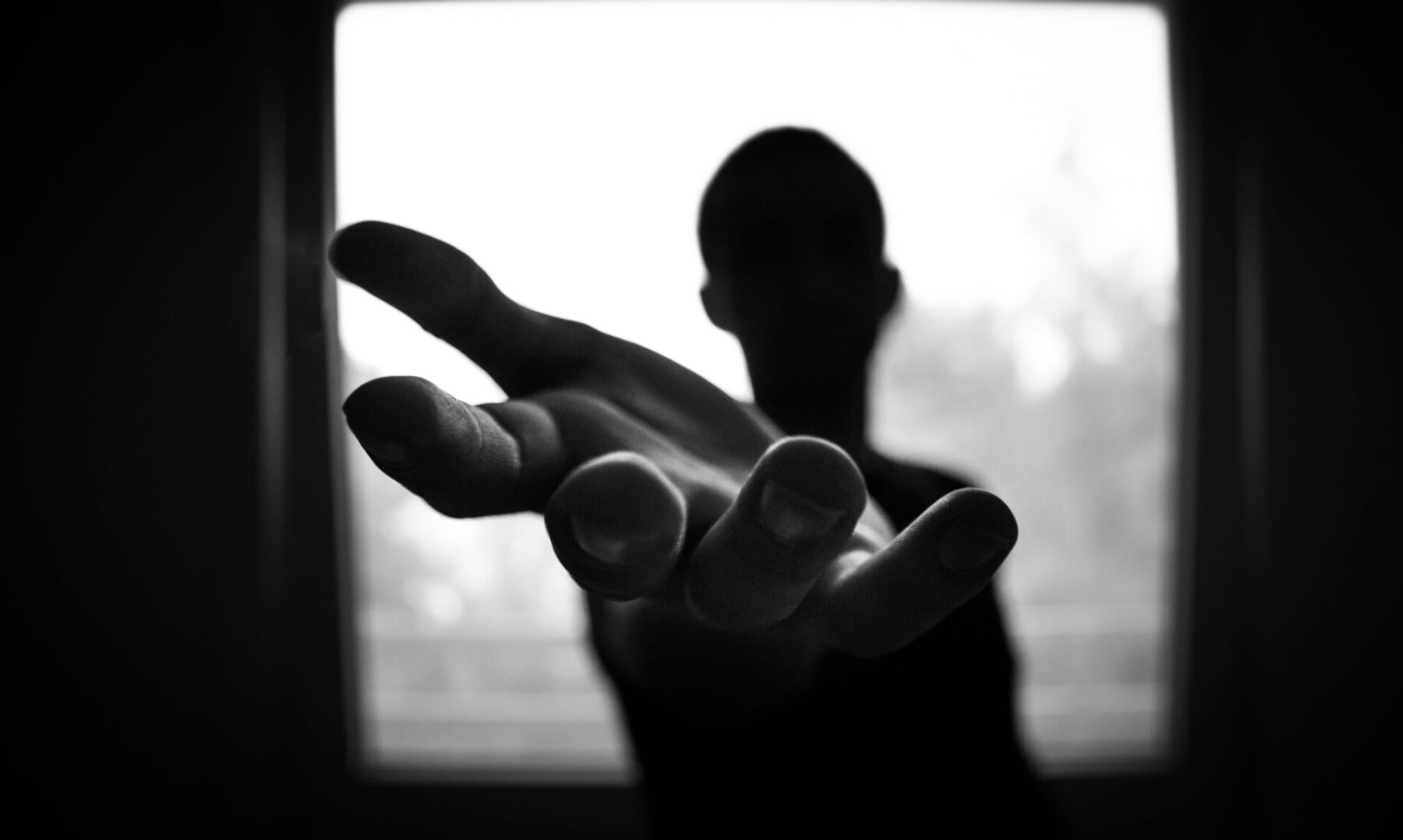 A person holding their hand out in front of a window.