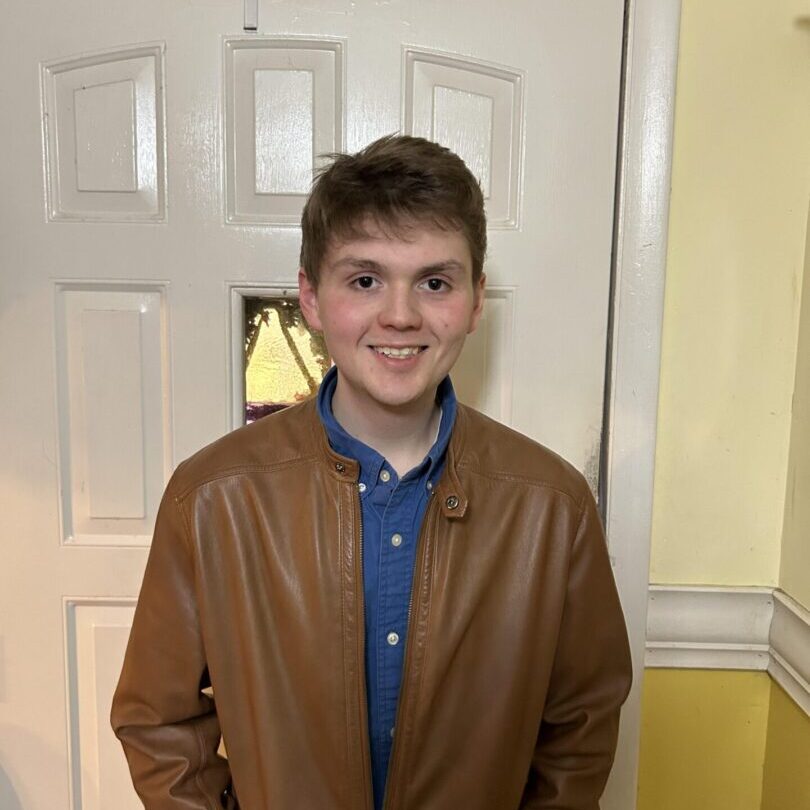 A young man in brown leather jacket standing next to door.